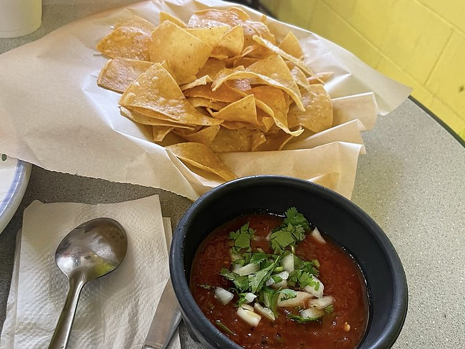 Chips and salsa on the table — Tortilla chips in the basket, salsa roja with onion and cilantro