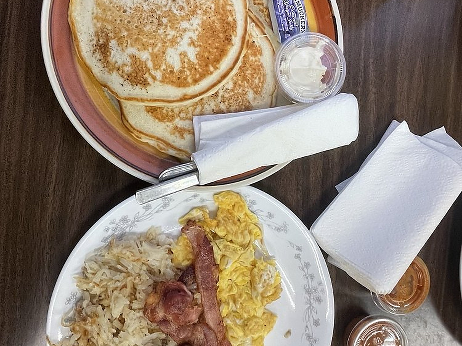 Breakfast at the table — Pancakes, scrambled eggs, bacon and hash browns on the plate